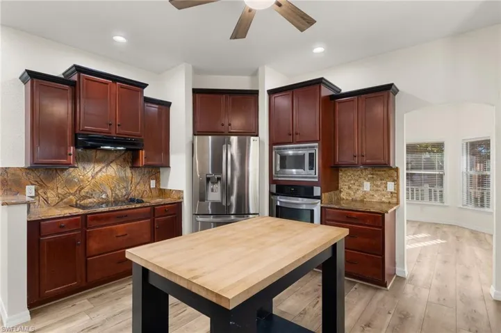 Kitchen featuring appliances with stainless steel finishes, tasteful backsplash, light hardwood / wood-style flooring, and light stone countertops
