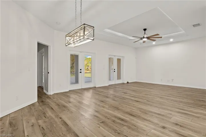 Unfurnished room featuring a raised ceiling, french doors, ceiling fan with notable chandelier, and light hardwood / wood-style flooring
