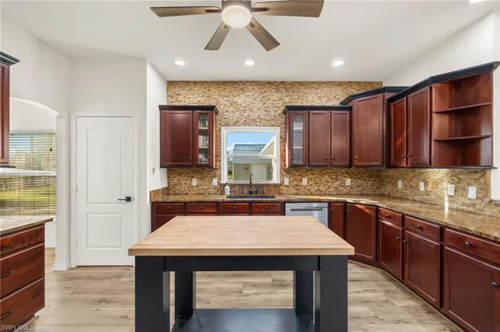 Kitchen with light stone counters, decorative backsplash, sink, dishwasher, and light hardwood / wood-style flooring