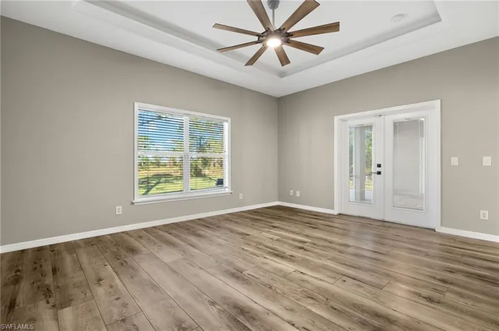 Spare room with plenty of natural light, a raised ceiling, light wood-type flooring, and french doors