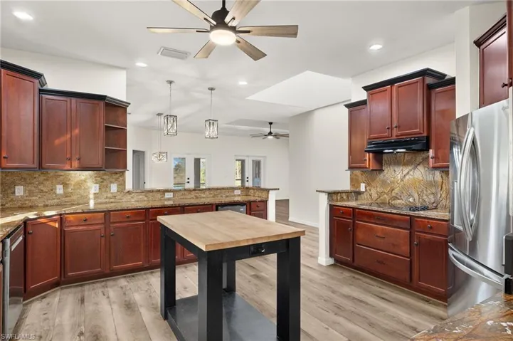 Kitchen featuring stainless steel appliances, backsplash, decorative light fixtures, light stone countertops, and light hardwood / wood-style flooring