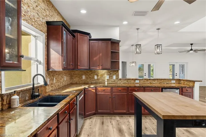 Kitchen with stainless steel dishwasher, light hardwood / wood-style floors, sink, and decorative light fixtures