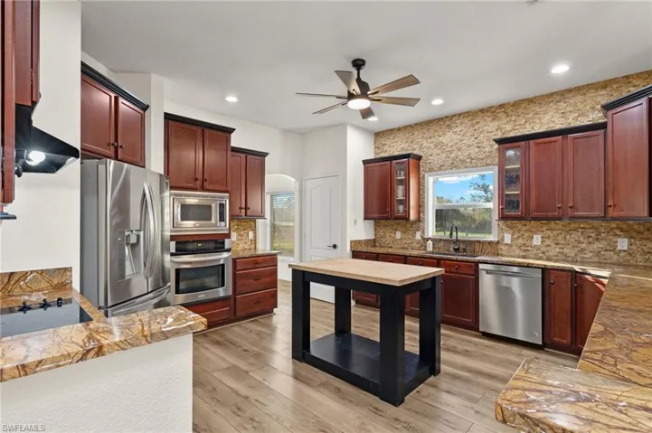 Kitchen featuring stainless steel appliances, sink, ceiling fan, backsplash, and light wood-type flooring