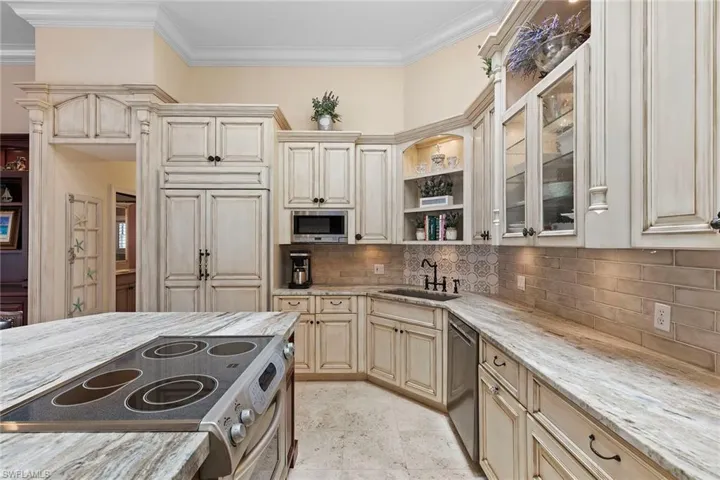 Kitchen featuring cream cabinets, appliances with stainless steel finishes, light stone counters, open shelves, and crown molding