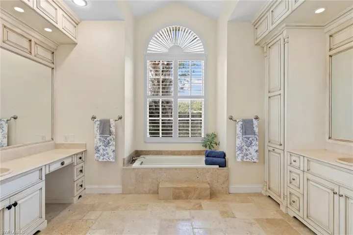 Bathroom featuring two vanities, a garden tub, vaulted ceiling, stone tile floors, and recessed lighting