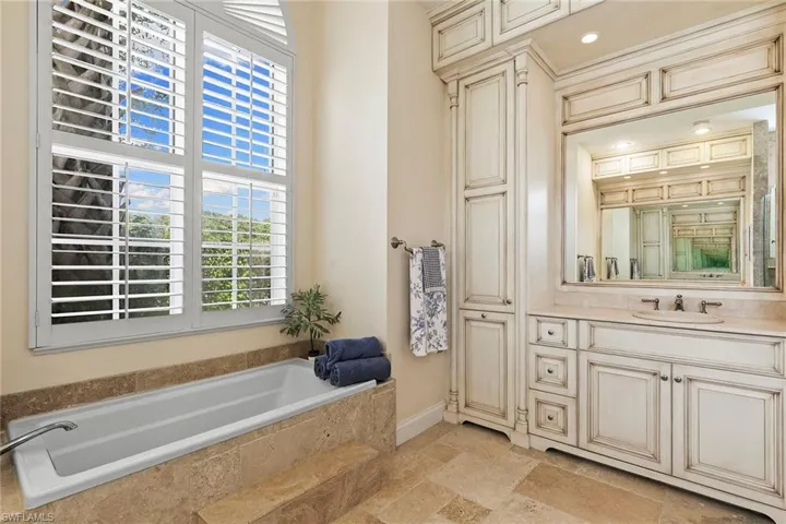 Bathroom with vanity, a garden tub, and stone tile flooring