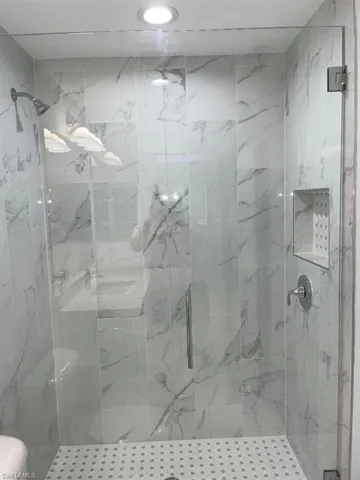 Glass-enclosed shower featuring white and gray marble-look tile, a built-in shower niche, chrome fixtures, and a recessed ceiling light