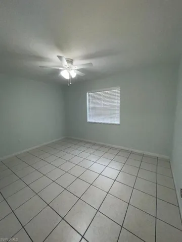 Neutral tone wall paint, a ceiling fan with integrated lighting, window with horizontal blinds, and square tile flooring