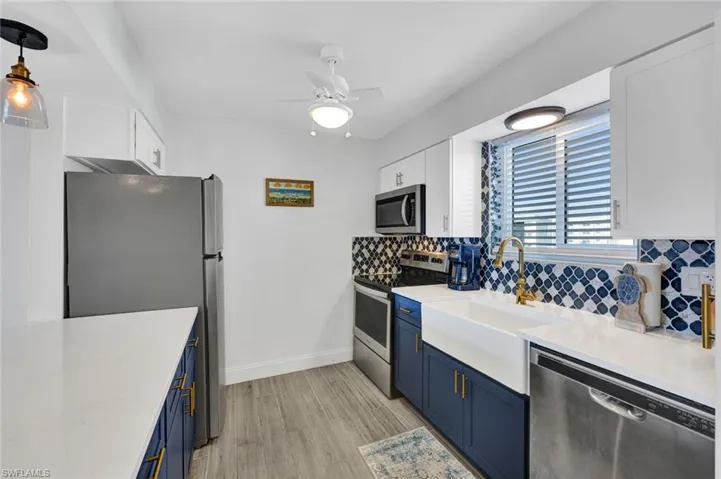 Kitchen featuring blue cabinets, white cabinets, appliances with stainless steel finishes, light wood finished floors, and tasteful backsplash