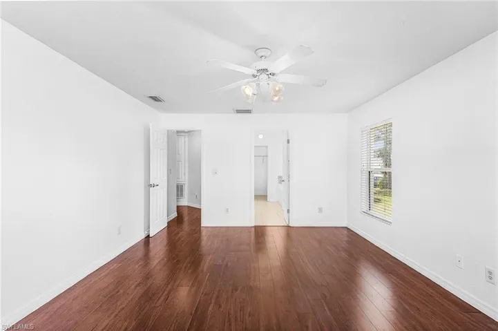 Wood-finish flooring, white walls, ceiling fan with integrated lighting, window with blinds, and white interior doors