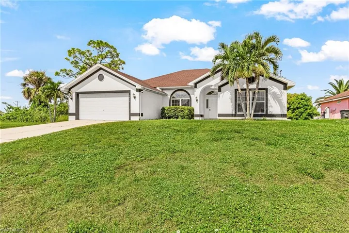 Single-story residence featuring a two-car garage, arched entry, and mature palm trees