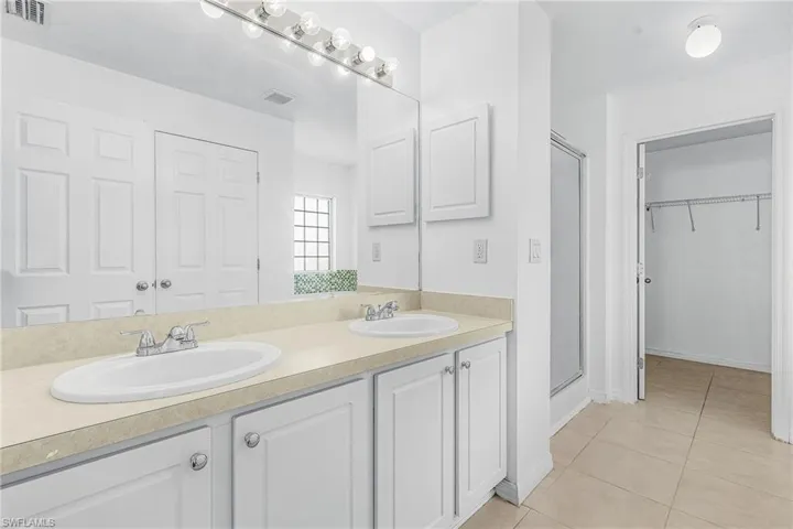 Dual vanity with white cabinetry, a large mirror, and overhead lighting