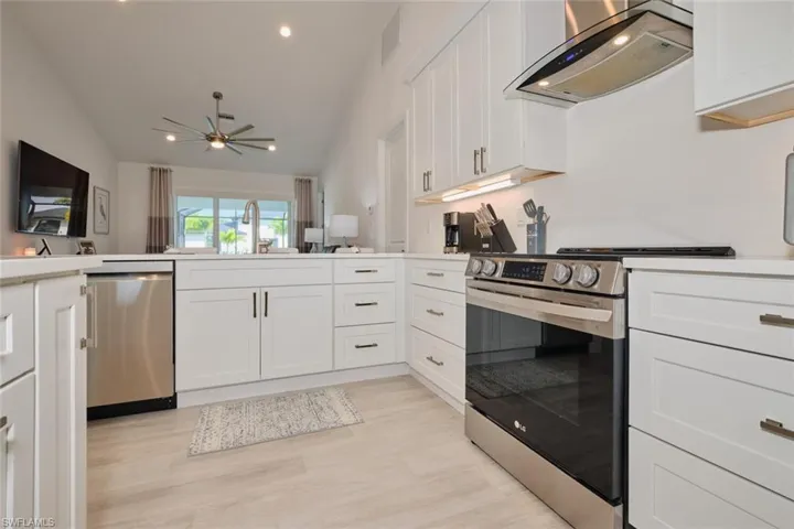Kitchen with white cabinets, stainless steel appliances, range hood, and vaulted ceiling