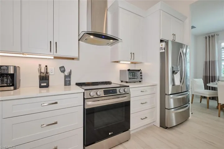 Kitchen featuring white cabinets, wall chimney exhaust hood, light hardwood / wood-style floors, and appliances with stainless steel finishes