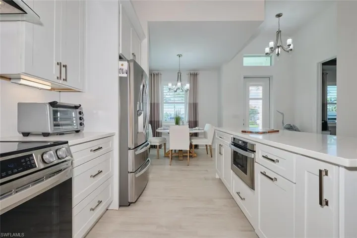 Kitchen featuring white cabinets, stainless steel appliances, hanging light fixtures, and an inviting chandelier
