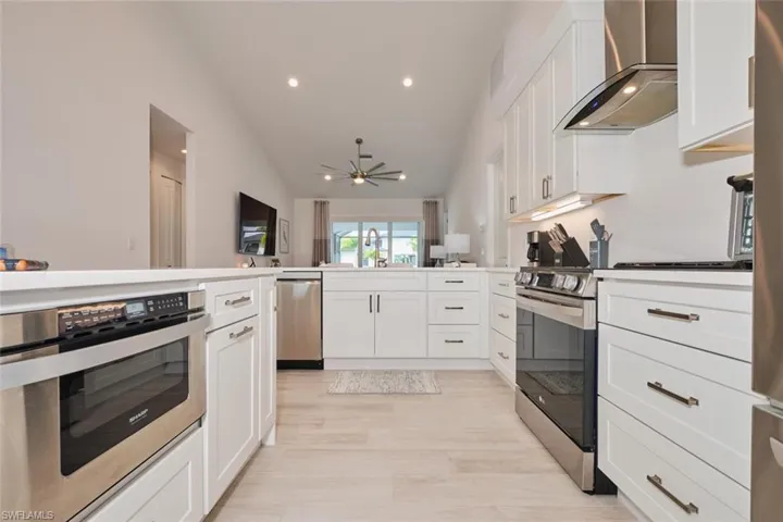 Kitchen with white cabinets, vaulted ceiling, wall chimney exhaust hood, ceiling fan, and stainless steel appliances