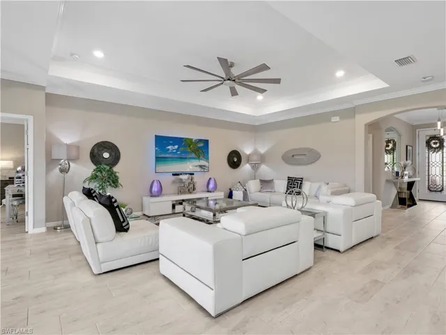 Living area with arched walkways, a tray ceiling, ornamental molding, ceiling fan, and recessed lighting