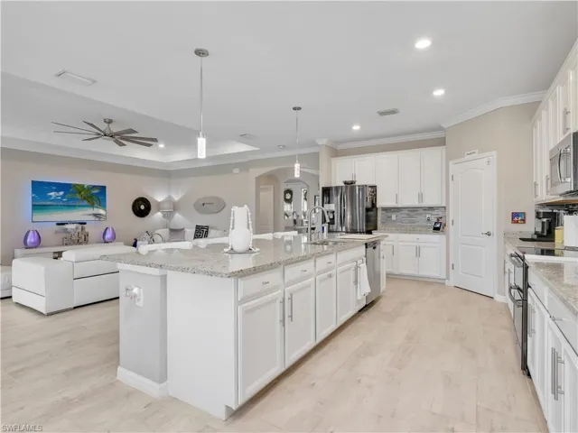 Kitchen with decorative light fixtures, arched walkways, open floor plan, white cabinetry, and decorative backsplash