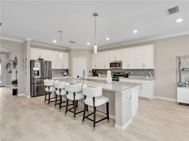 Kitchen with a breakfast bar, backsplash, stainless steel appliances, white cabinets, and a large island