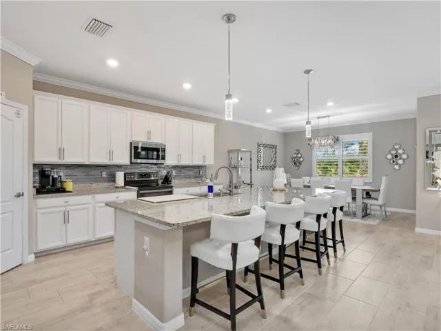 Kitchen with ornamental molding, a kitchen bar, decorative backsplash, pendant lighting, and white cabinetry