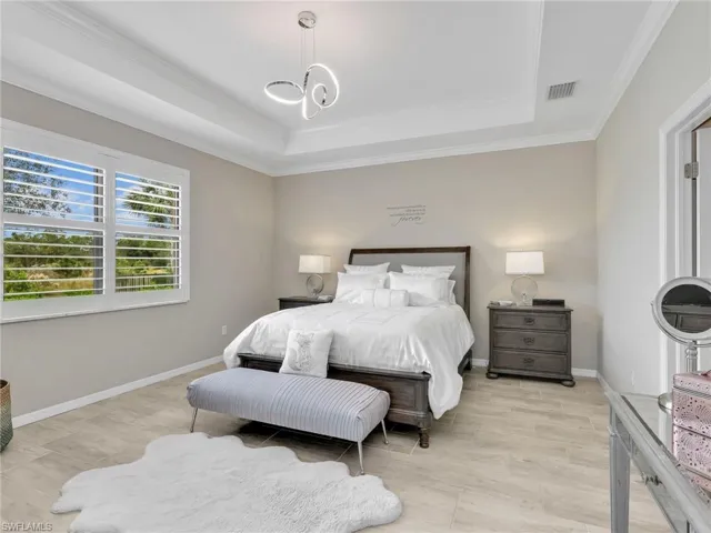 Bedroom featuring a tray ceiling, ornamental molding, wood tiled floors, and a chandelier