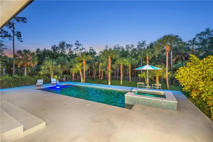 Pool at dusk featuring an in ground hot tub and a patio