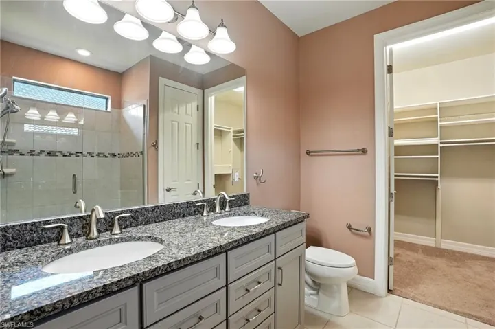Full bathroom featuring a walk in closet, light tile patterned flooring, a shower stall, and double vanity