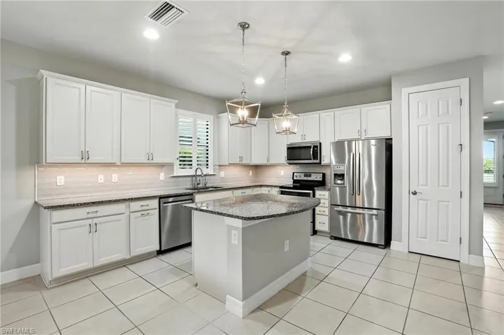Kitchen with appliances with stainless steel finishes, dark stone counters, white cabinets, decorative light fixtures, and recessed lighting