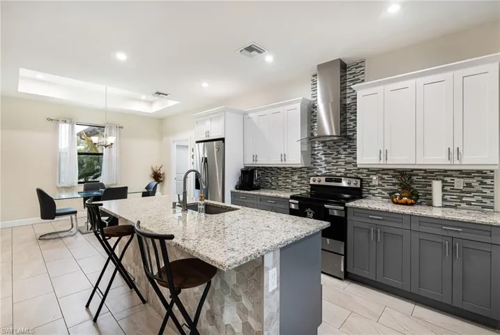 Kitchen featuring wall chimney exhaust hood, white cabinets, appliances with stainless steel finishes, and a kitchen island with sink