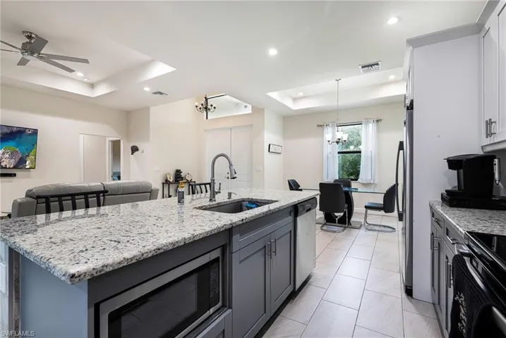 Kitchen with appliances with stainless steel finishes, ceiling fan with notable chandelier, a raised ceiling, a kitchen island with sink, and sink