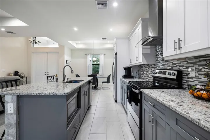 Kitchen with wall chimney exhaust hood, white cabinetry, sink, and stainless steel appliances