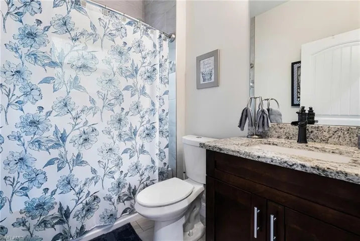 Bathroom with a shower with curtain, vanity, tile patterned flooring, and toilet