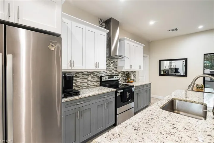 Kitchen with sink, white cabinets, wall chimney range hood, stainless steel appliances, and light stone countertops