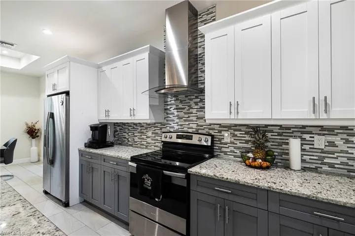 Kitchen with light stone counters, white cabinets, tasteful backsplash, wall chimney exhaust hood, and appliances with stainless steel finishes