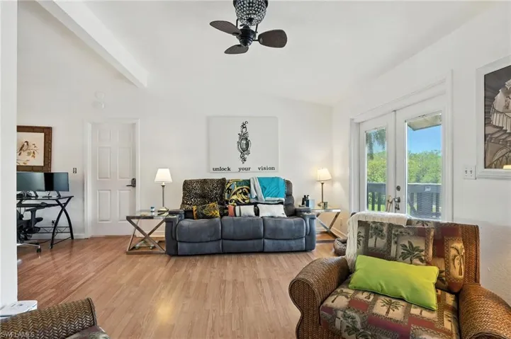 Living area featuring vaulted ceilings, wood-finish flooring, a ceiling fan with a decorative light fixture, and French doors opening to an outdoor space