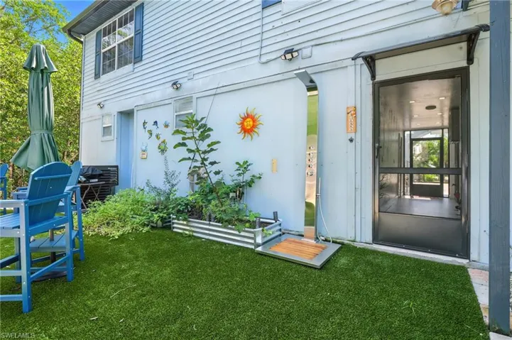 Rear exterior featuring artificial turf, a screen door entrance, and a corrugated metal planter box