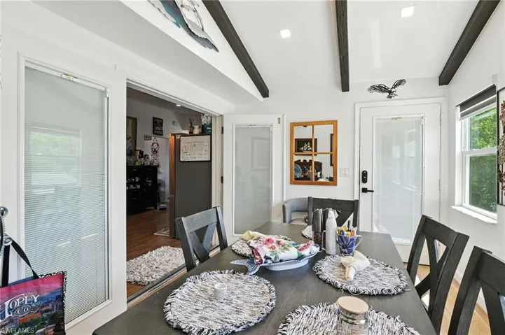 Dining area featuring exposed ceiling beams, a white paneled door with integrated blinds, and ample natural light from multiple windows