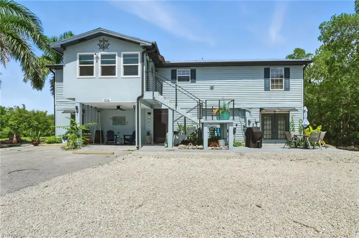 Two-story residence featuring light blue siding, an exterior staircase with metal railings, a covered carport area with a ceiling fan, and a ground-level patio with double french doors