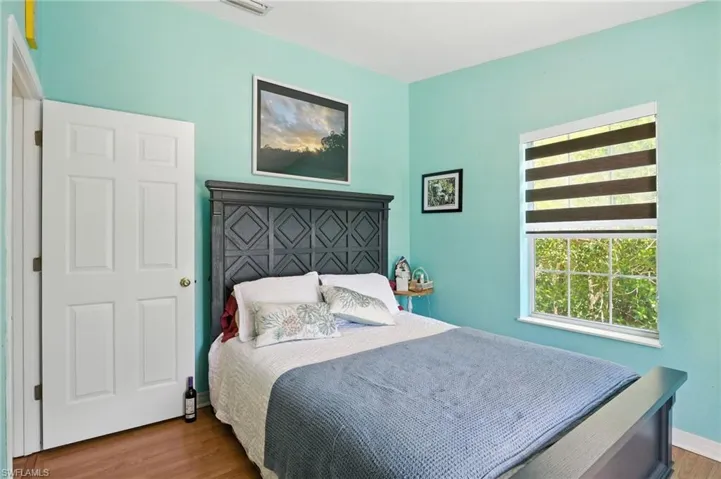 Spacious room featuring a white paneled door, wood-finish flooring, and a window with horizontal blinds