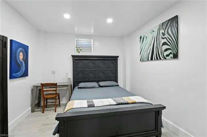 Bright room featuring recessed lighting, a dark wood-finish bed frame, light wood-look flooring, white walls, and a high window