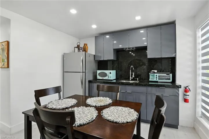 Compact kitchen area featuring sleek grey cabinetry, a black stone countertop with matching backsplash, and a stainless steel refrigerator