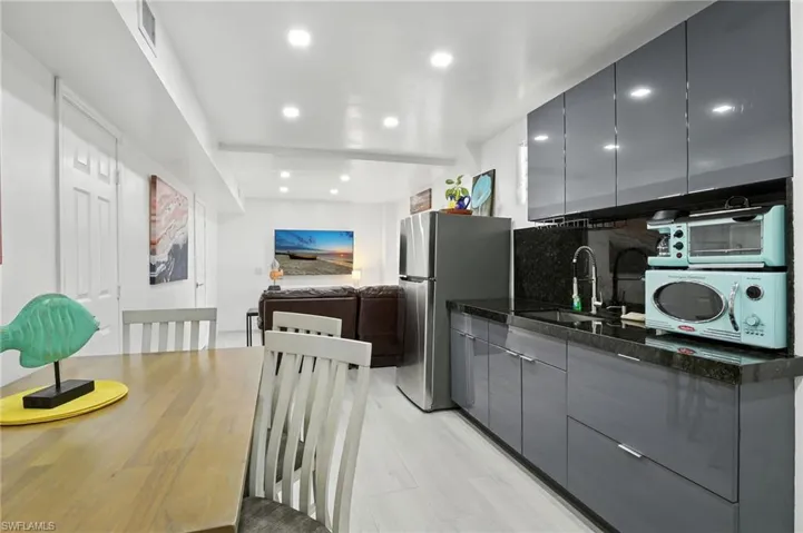 Modern kitchen area featuring dark gray flat-panel cabinetry with a polished finish, dark stone countertops, and a stainless steel refrigerator