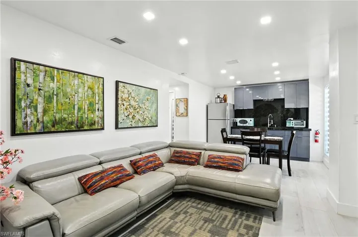 Open-concept living area featuring light wood-finish flooring, recessed lighting, and a modern kitchen with sleek gray cabinetry and dark countertops