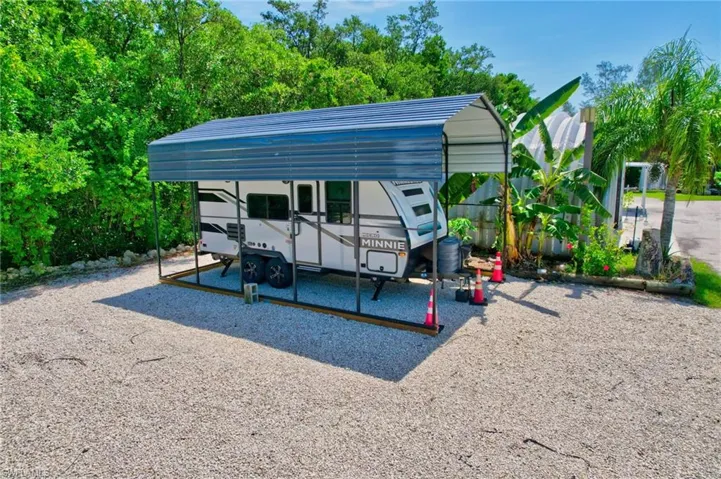 Gravel lot featuring a metal carport structure with a corrugated roof