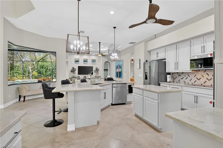 Kitchen with ceiling fan, open floor plan, arched walkways, and light stone countertops