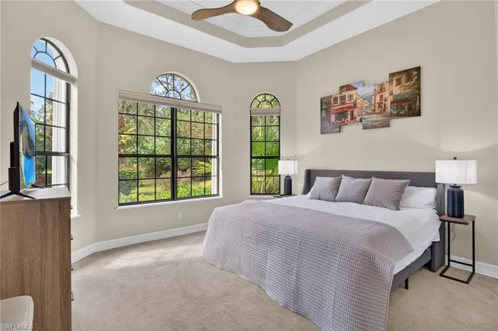 Carpeted bedroom featuring ceiling fan, ornamental molding, and a raised ceiling
