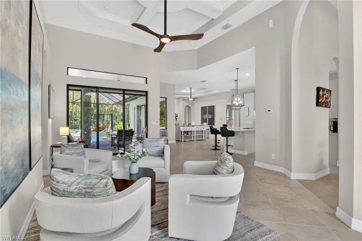 Living area featuring coffered ceiling, a ceiling fan, arched walkways, and light tile patterned flooring