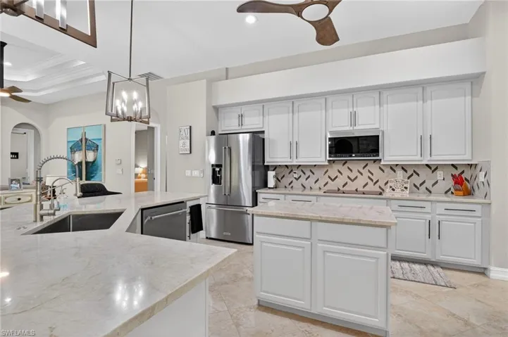Kitchen with ceiling fan, a kitchen island, white cabinets, light stone countertops, and stainless steel appliances