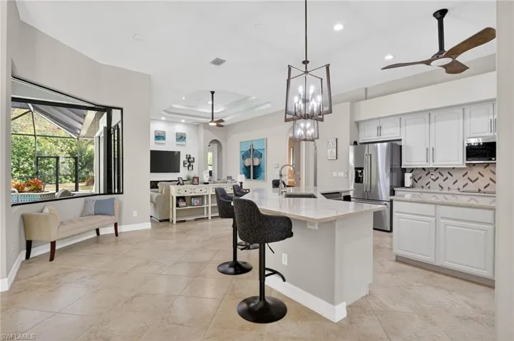 Kitchen with a ceiling fan, open floor plan, a kitchen bar, tasteful backsplash, and a tray ceiling
