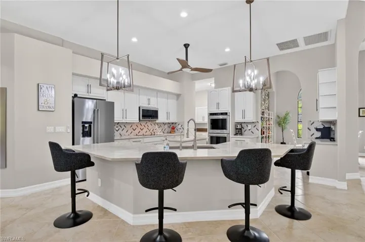 Kitchen with suspended lighting, white cabinetry, tasteful backsplash, a breakfast bar, and a spacious island